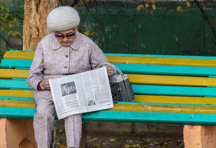 Donna anziana sulla panchina mentre legge il giornale